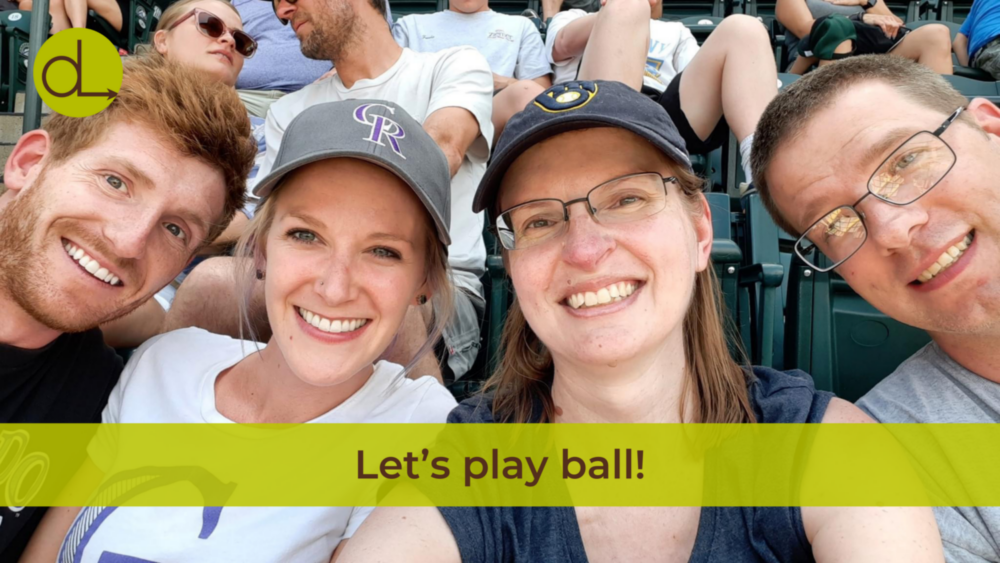 Kara and Jill smiling for a selfie with their spouses at a baseball game.